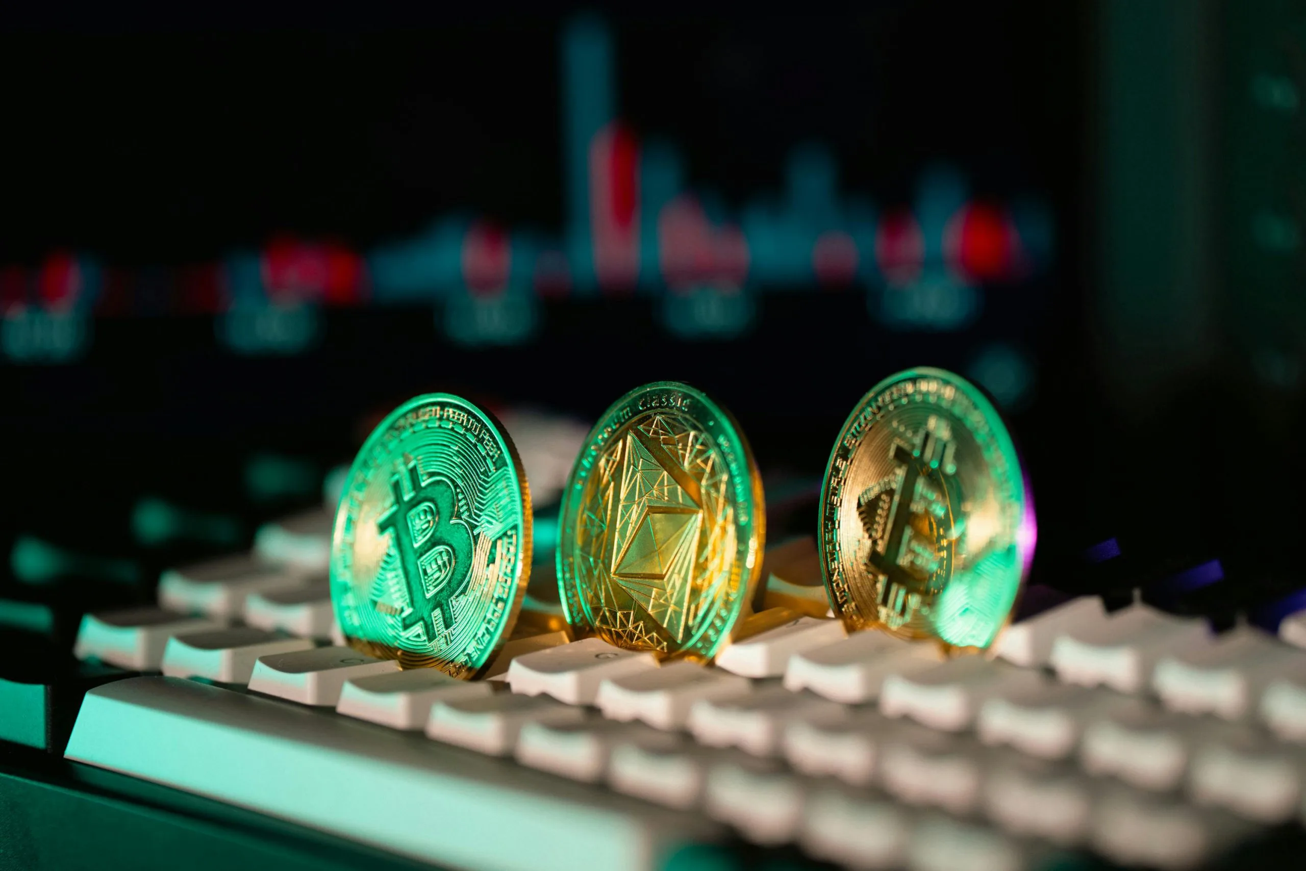 Close-up of Bitcoin and Ethereum coins placed on a keyboard, with market charts in the background.