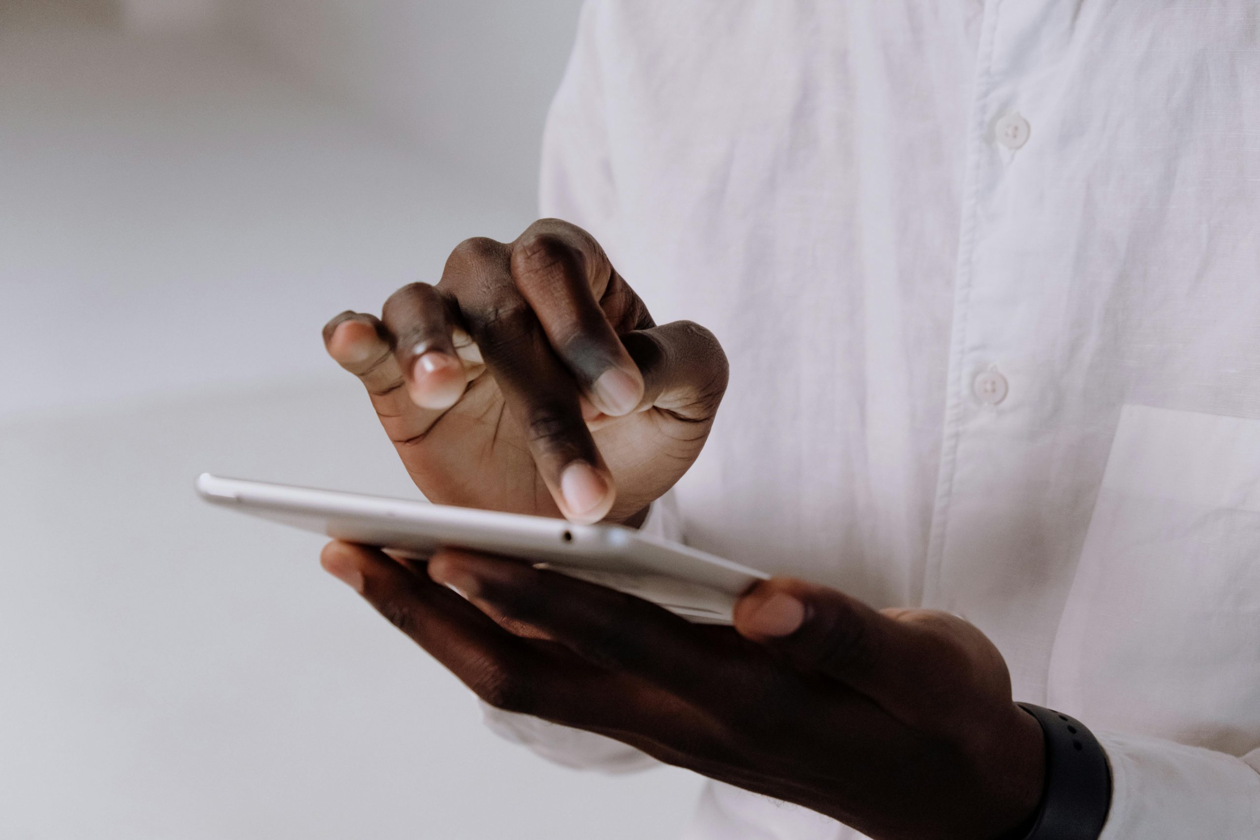 Adult using touchscreen tablet in white shirt, emphasizing technology and communication.